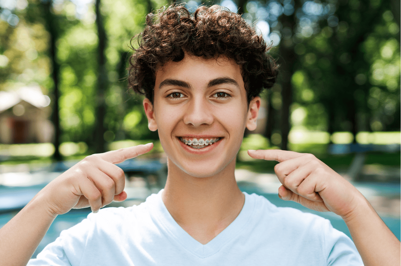 Teenager smiling and pointing to traditional metal braces.